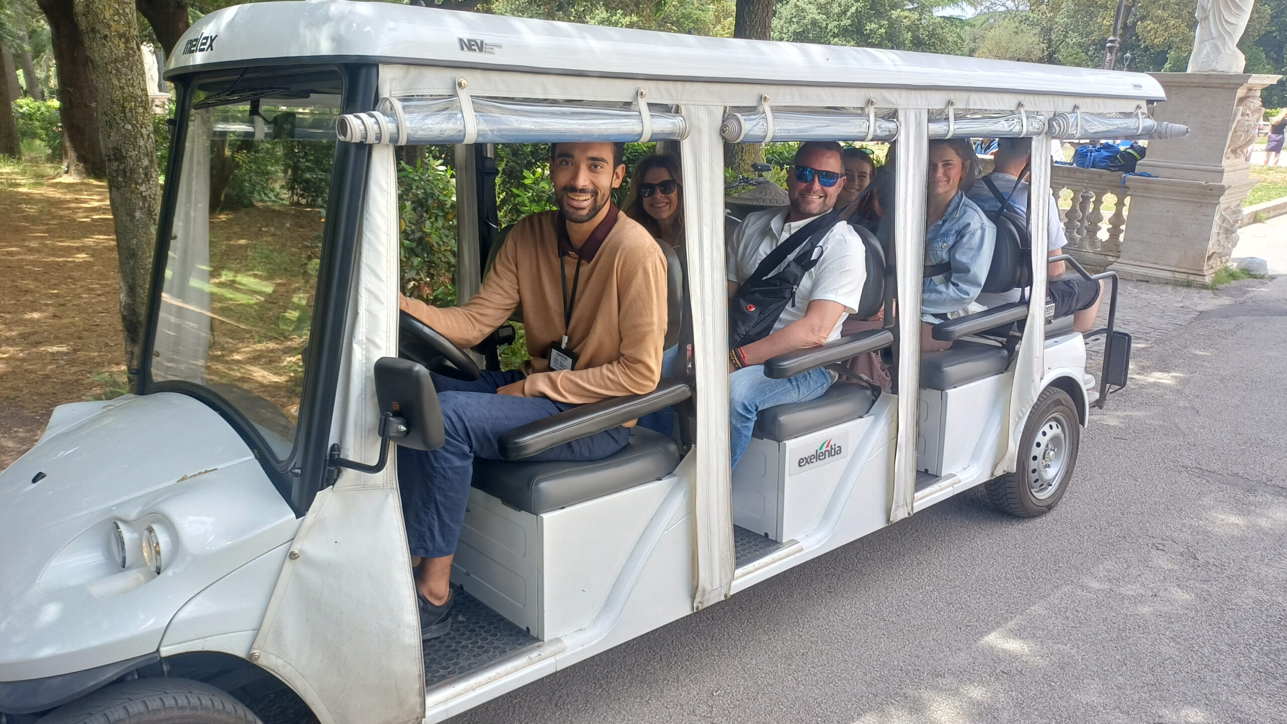 Smiling local guide driving guests on an electric golf cart tour through the leafy Villa Borghese gardens in Rome
