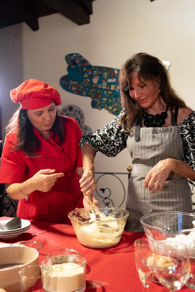 Chef in red guiding a guest mixing tiramisu cream in a glass bowl