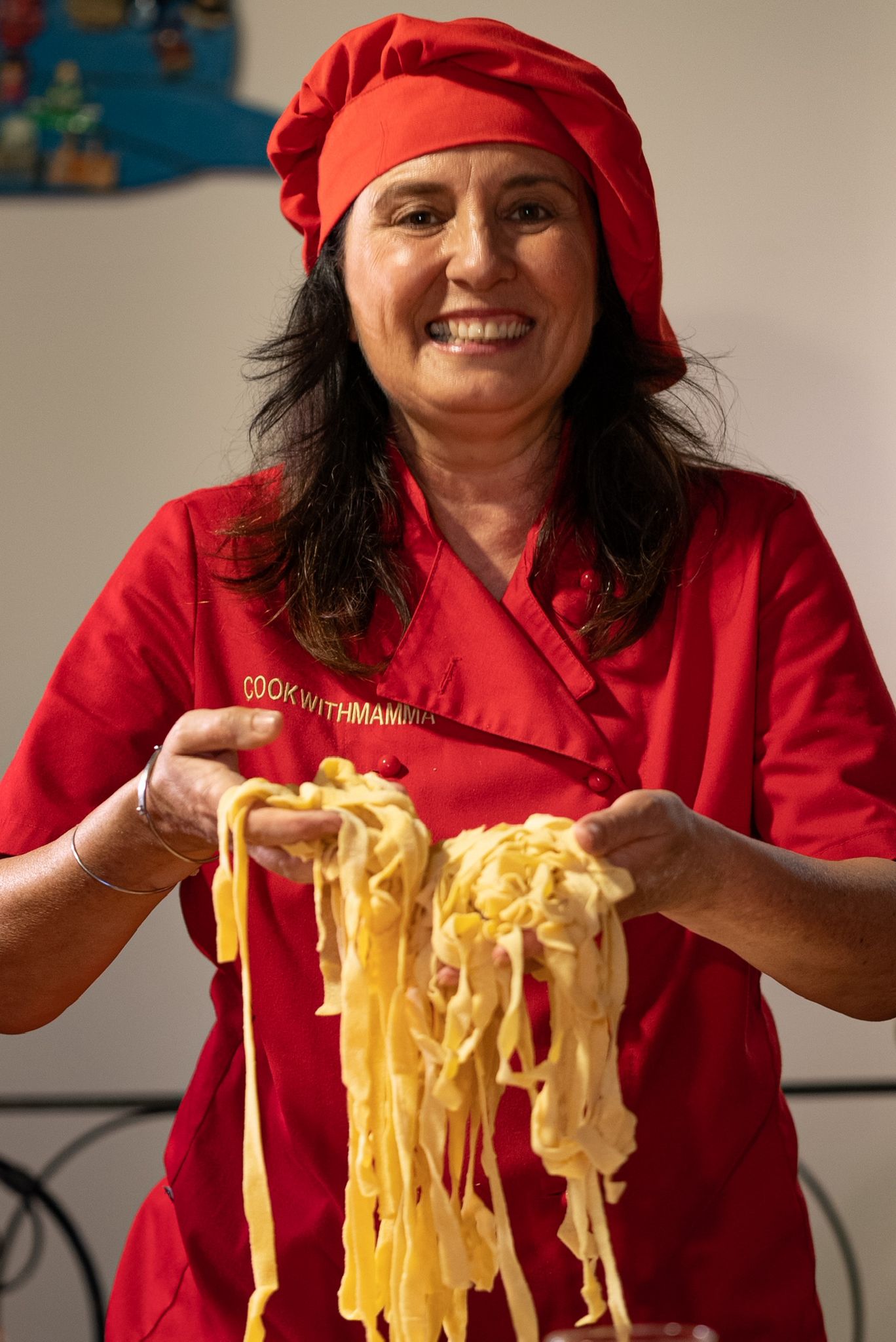 Smiling chef in a red uniform holding freshly made tagliatelle