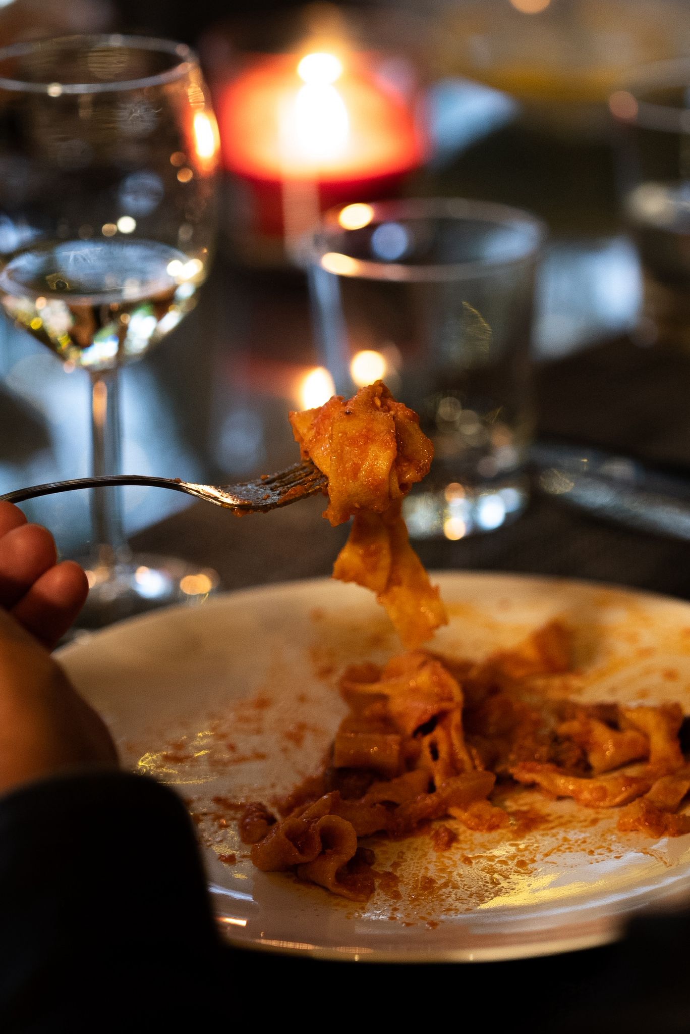 A guest twirling fresh pasta on a fork at a candlelit table