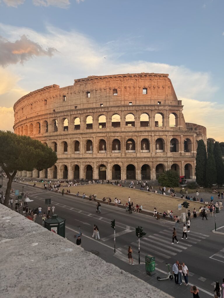 The Colosseum glowing at sunset under pink clouds, seen from the hill above the meeting point