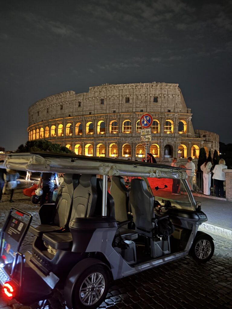 Guests in a golf cart in front of the Colosseum at night